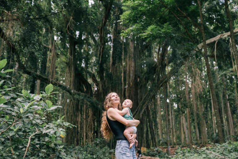 A joyful mother holding her baby amidst a lush green forest, enjoying nature.